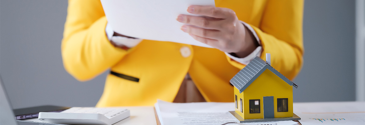 Mujer revisando documentos de financiamiento hipotecario junto a maqueta de casa representando los retos del crédito hipotecario tradicional para comprar vivienda en México